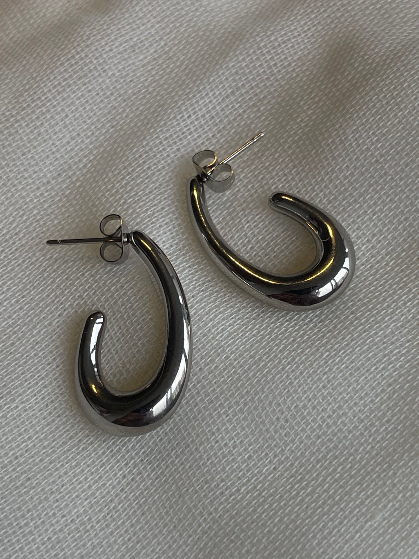 Brincos Clúsia prateados com design curvo em aço inoxidável.