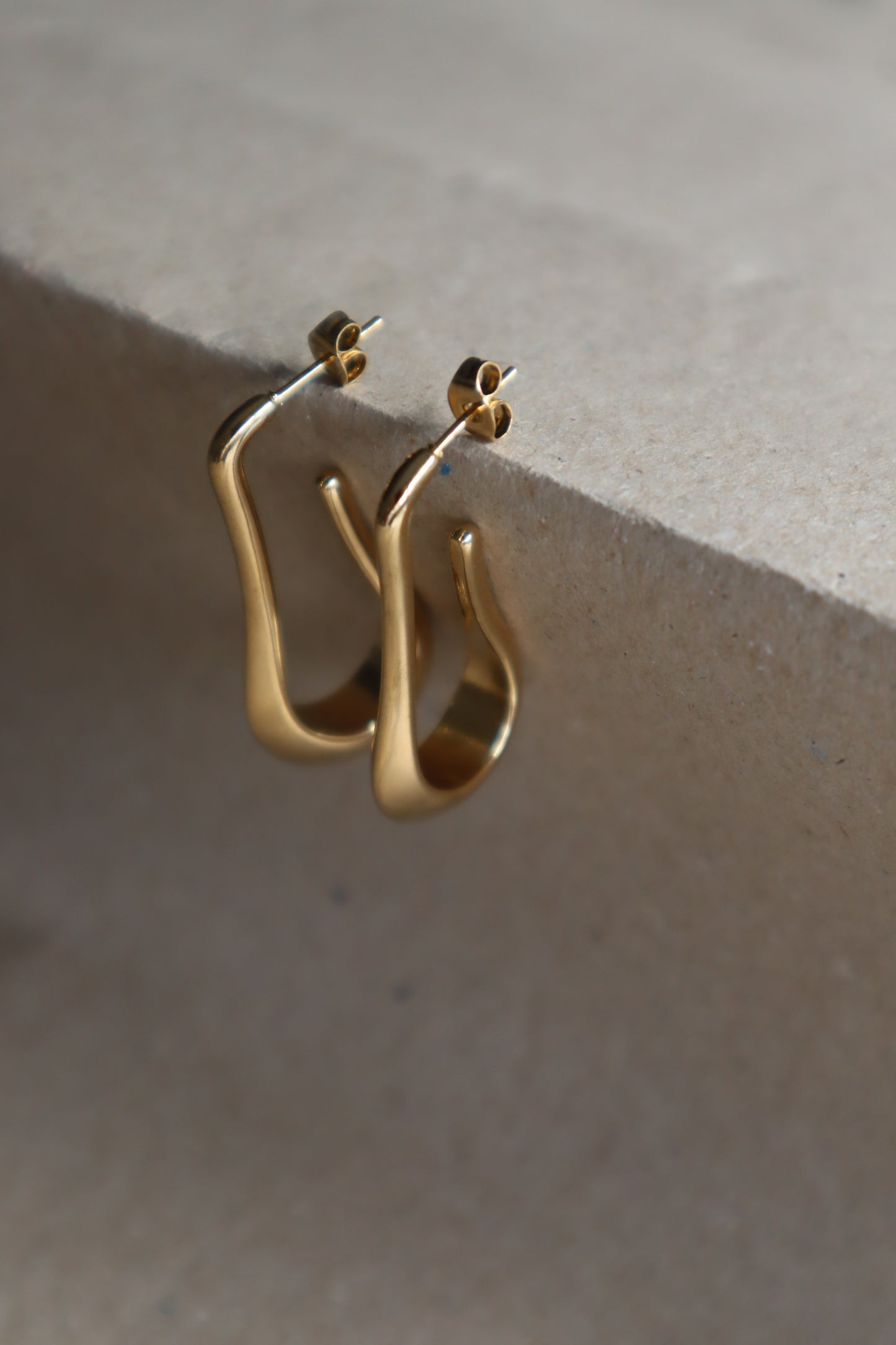 Brincos Érica em aço inoxidável dourado com design minimalista e alongado.