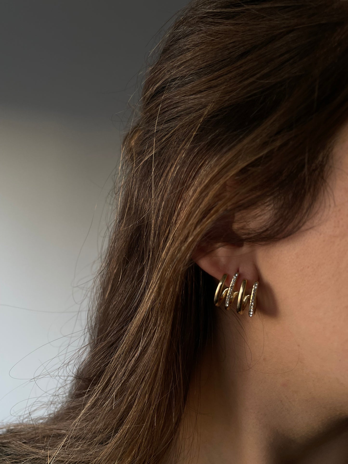 Brincos Flor de Mel, dourados, sofisticados, com quatro aros que alternam entre textura polida e com alguns cristais