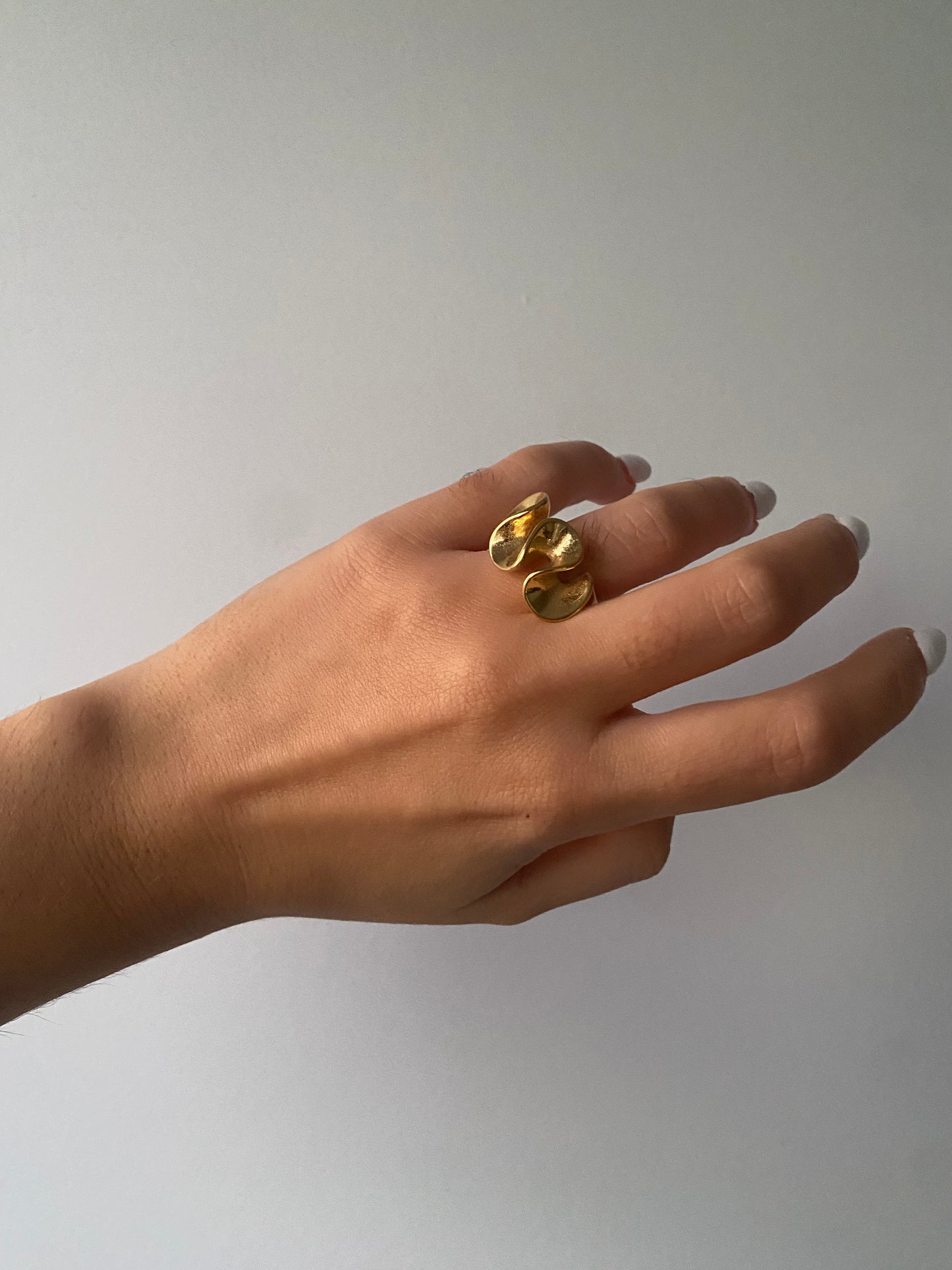 Anel Loureiro volumétrico em aço inoxidável dourado com design curvo.