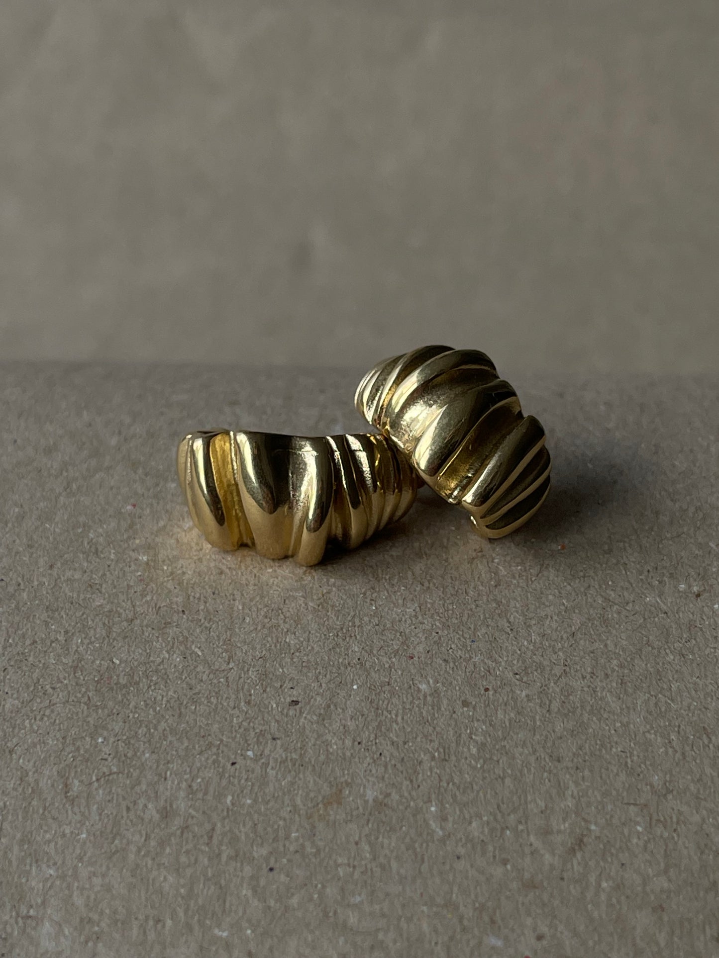 Brincos Melissa em aço inoxidável dourado com design ondulado e robusto.