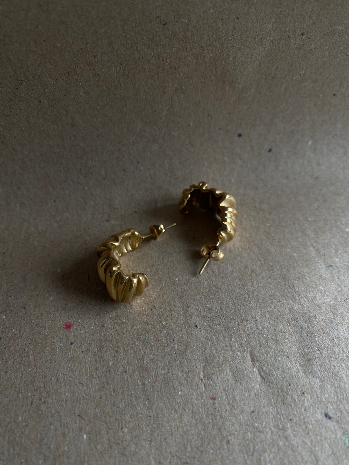 Brincos Melissa em aço inoxidável dourado com design ondulado e robusto.