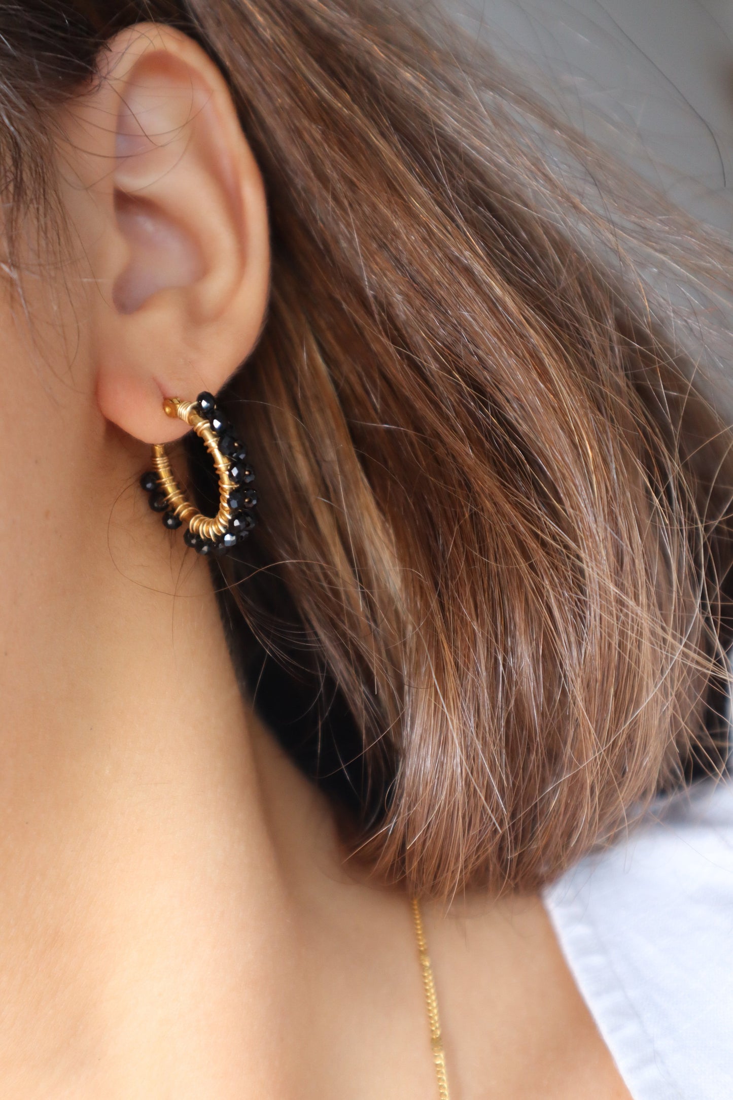 Brincos Arruda em argola dourada com pedras pretas em aço inoxidável.