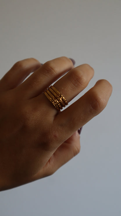 anel Amie dourado com múltiplos aros e textura rugosa em aço inoxidável