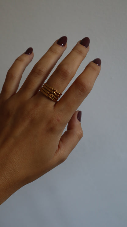 anel Amie dourado com múltiplos aros e textura rugosa em aço inoxidável