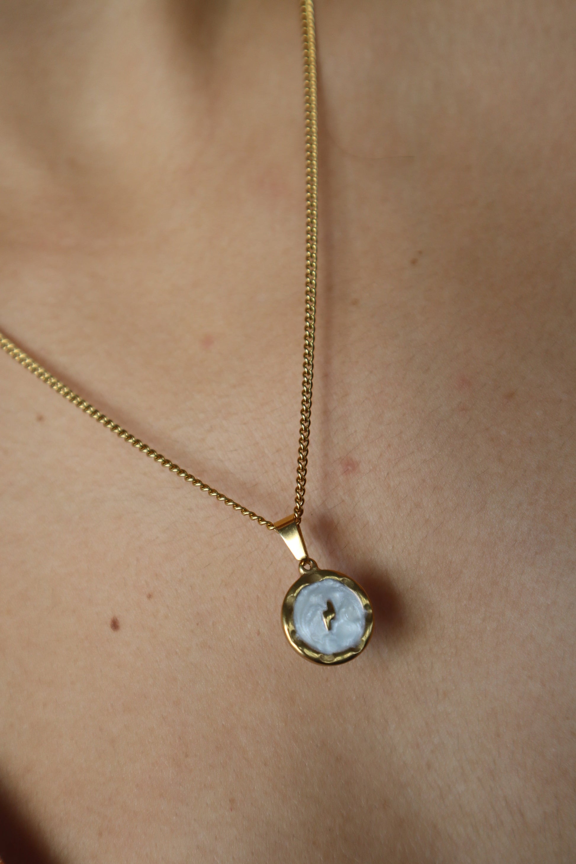 Corrente dourada com pendente redondo com um raio em fundo branco